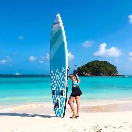 Woman holding the blue and white FatStick 12'6 Inflatable Touring Paddle Board SUP on a sandy beach foreground and turquoise ocean background