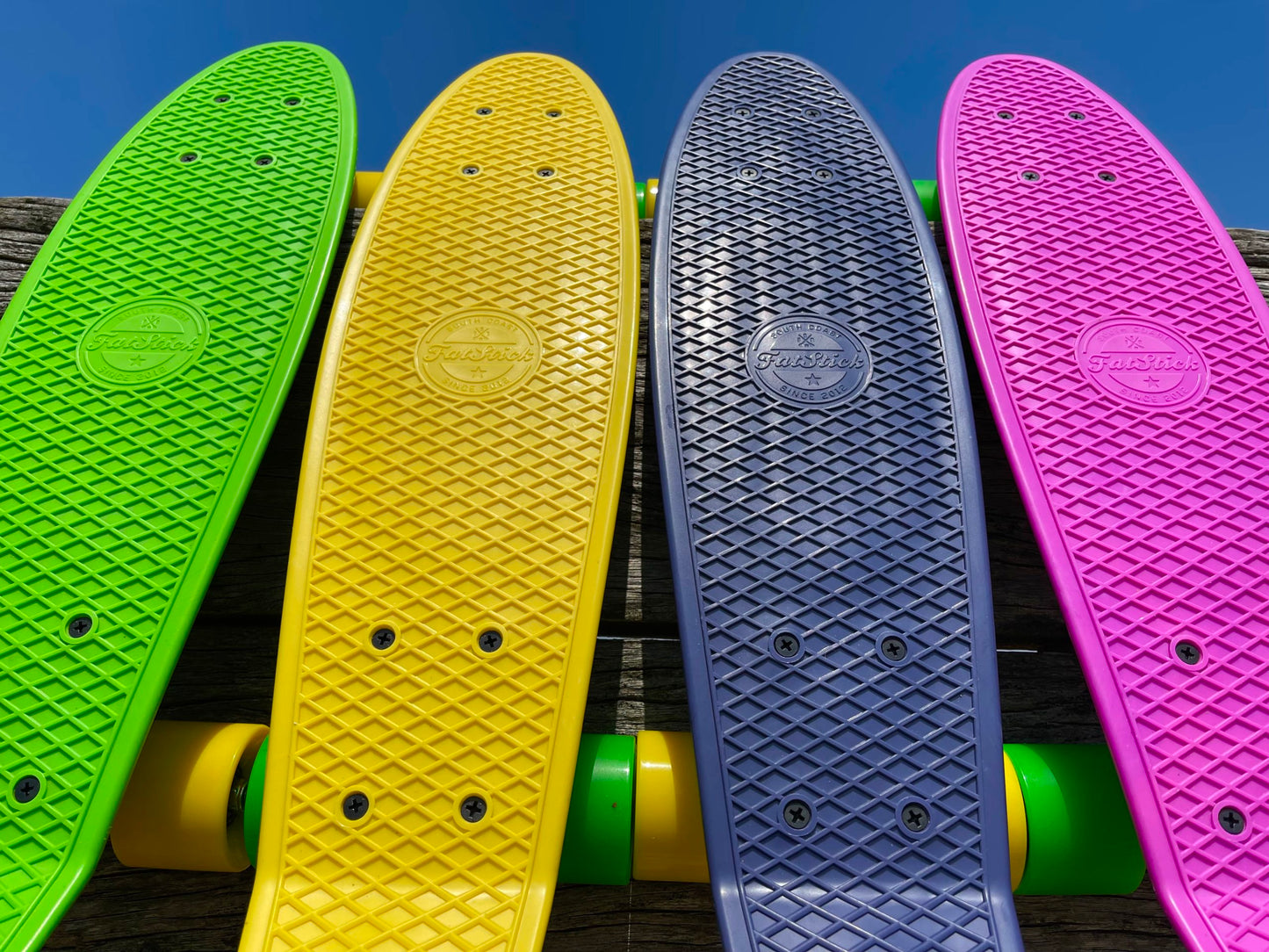 Upward view of four colorful FatStick Mini-Cruiser skateboards decks and wheels against blue sky