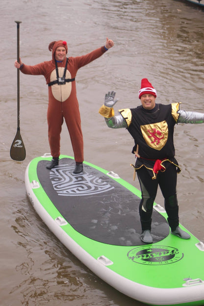 Two men in costumes, one dressed as a bear and one as a knight, standing on a green and black standing paddle board in the water.