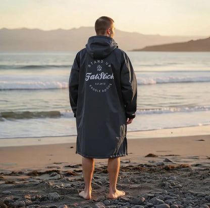Rear view of a man in a grey FatWrap recycled fleece changing robe looking out at the ocean at sunset.