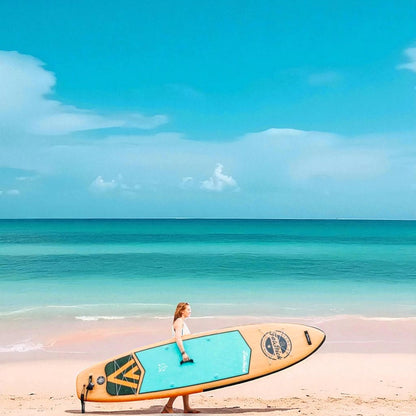 Woman carrying the FatStick Wooden Menace 11'2 inflatable paddle board across a sandy beach towards a calm, turquoise ocean.