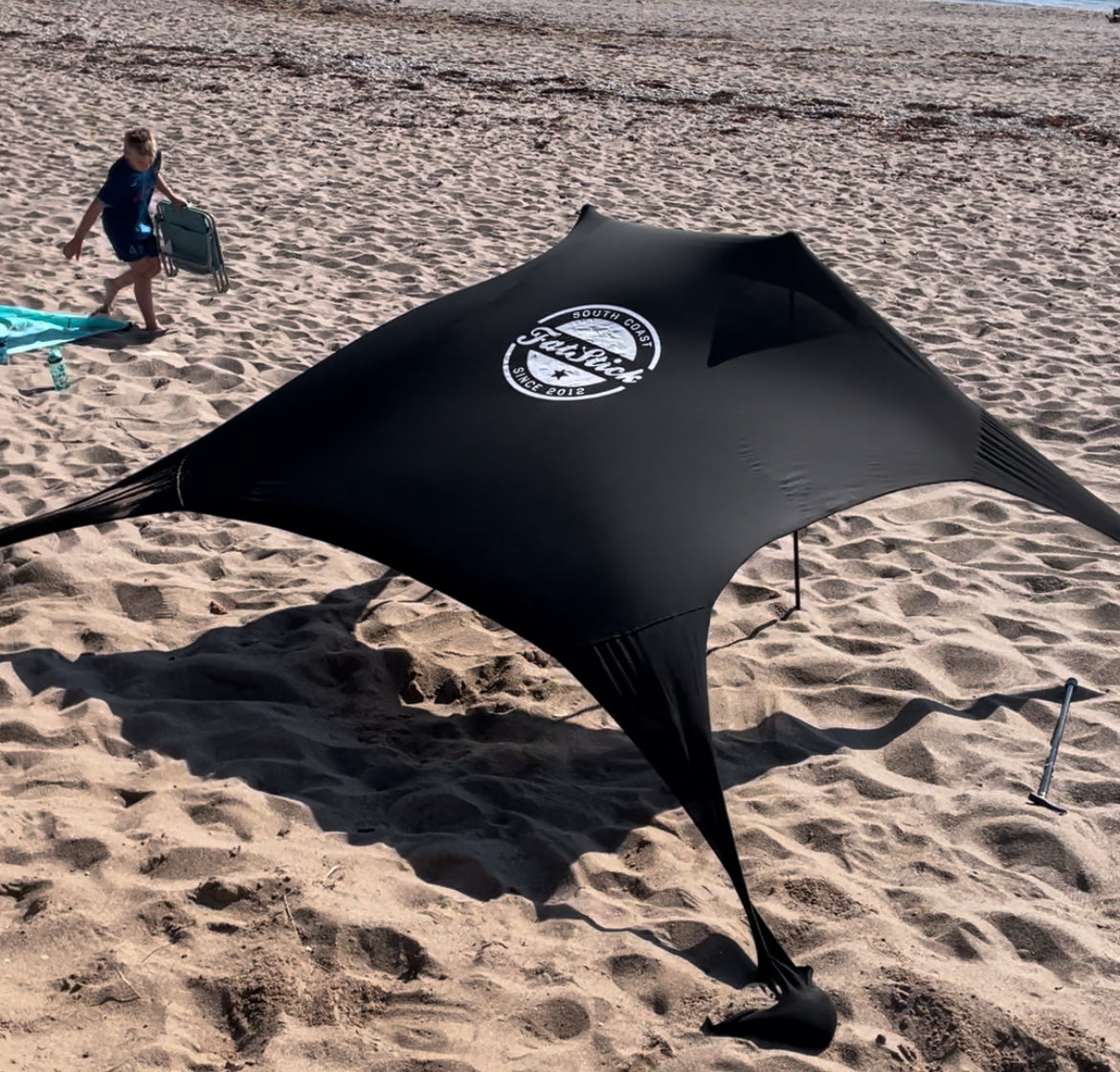 Black Fatstick Beach Tent sun shade set up on a sandy beach with a child in the background.