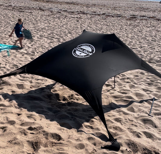 Black Fatstick Beach Tent sun shade set up on a sandy beach with a child in the background.