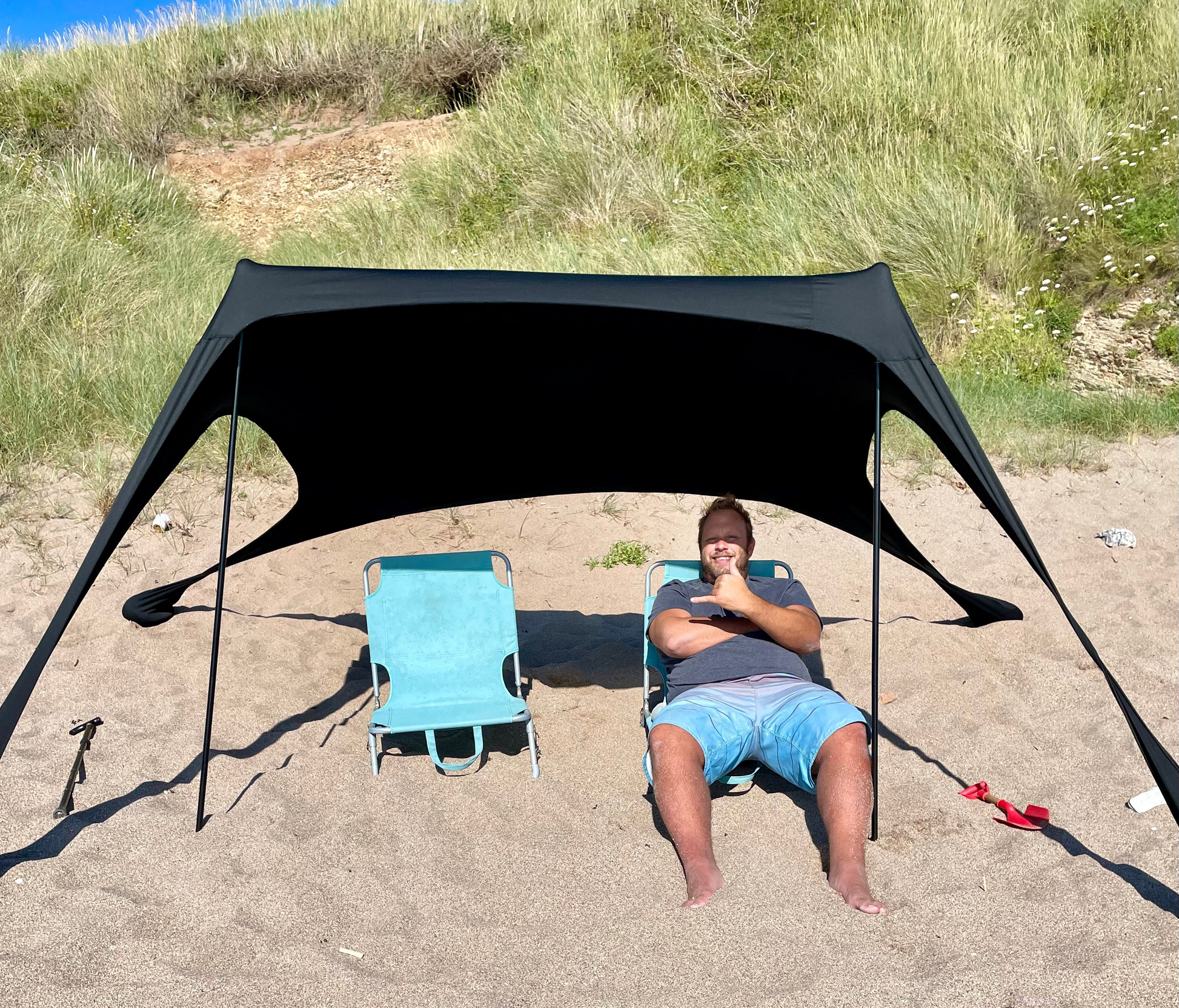 Man and blue beach chair under a black Fatstick Beach Tent sun shade on a sandy beach.