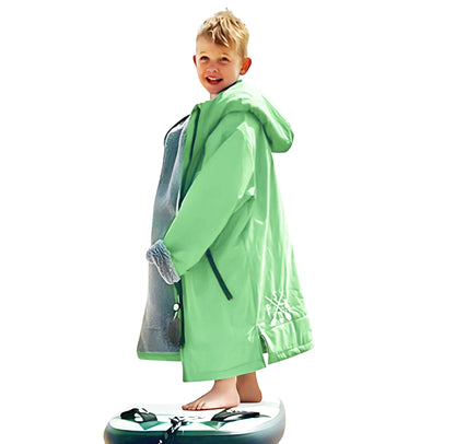 Young boy in green FatStick Kids FatWrap changing robe with sherpa fleece lining, smiling, on paddleboard.