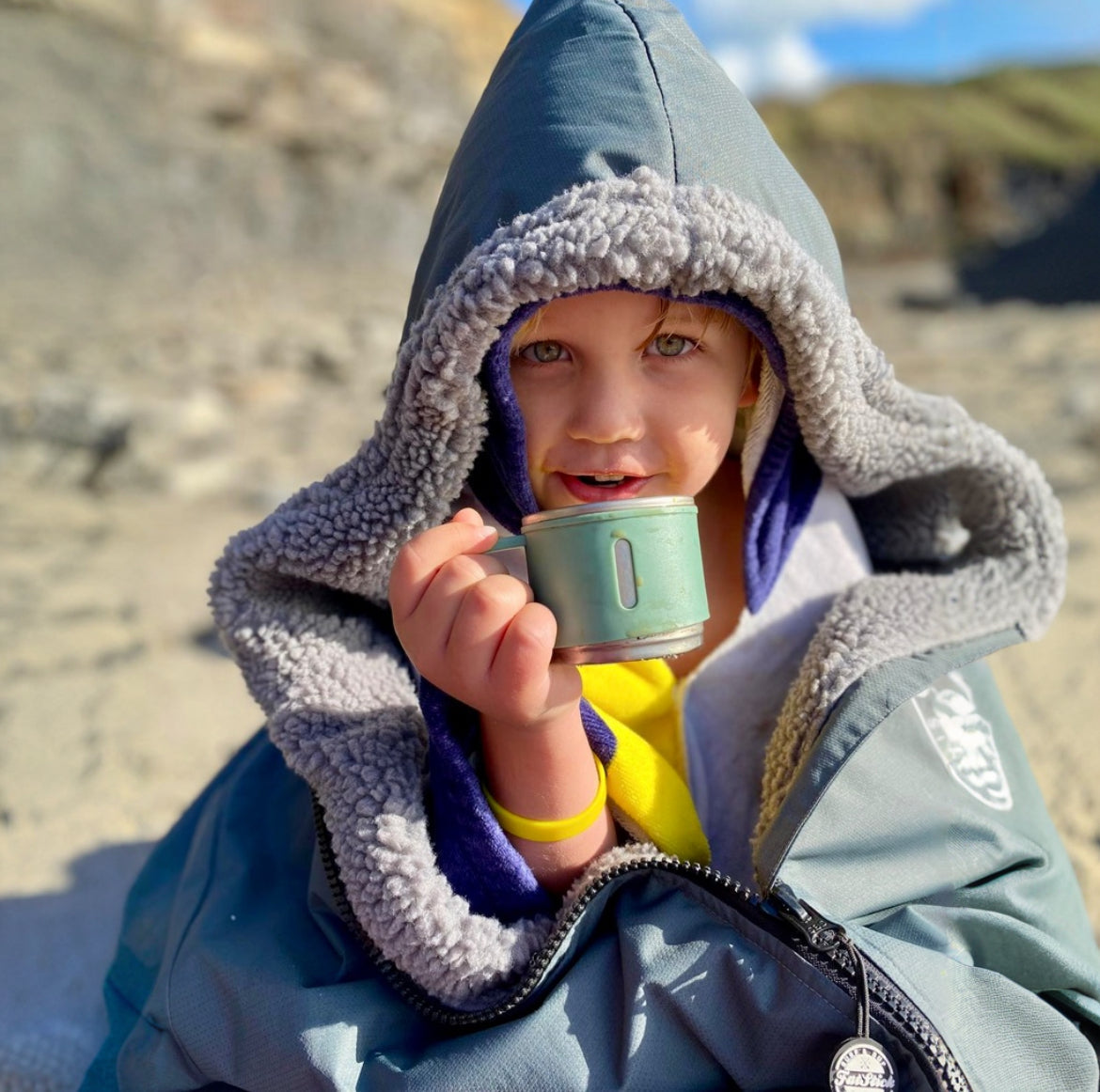 Close up of child in grey FatStick Kids FatWrap robe with sherpa fleece lining, holding mug.