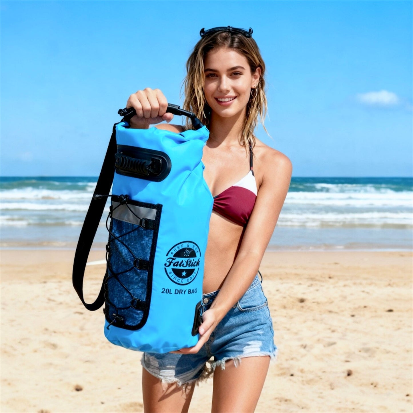 Woman on a beach holding a blue 20Ltr FatStick Dry Bag & Backpack, showcasing its size and portability.