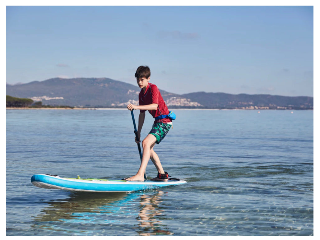 Young male paddler on a blue Fatstick Gromstick inflatable paddle board on calm clear water.