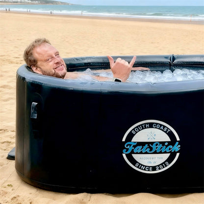 Man in cold water therapy plunge pool on beach, ice bath filled with ice cubes, making shaka sign.