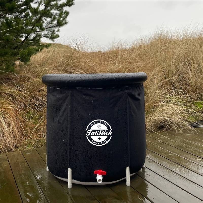 Black FatStick Recovery Ice Bath outdoors on a wooden deck surrounded by tall dry grass.