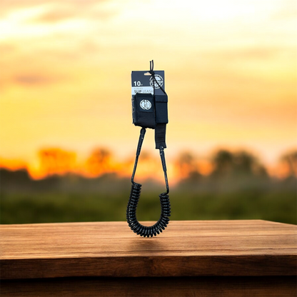 FatStick Boards 10ft black coiled SUP ankle leash against a sunset background