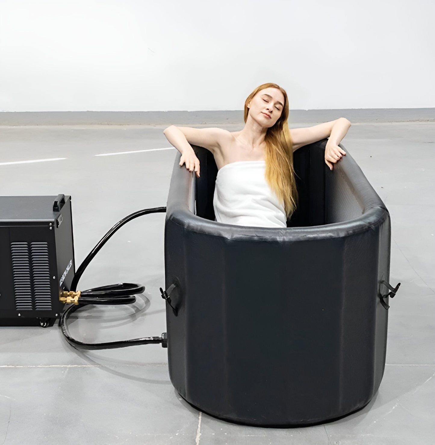 Woman relaxing in an inflatable ice bath connected to the black home chiller unit