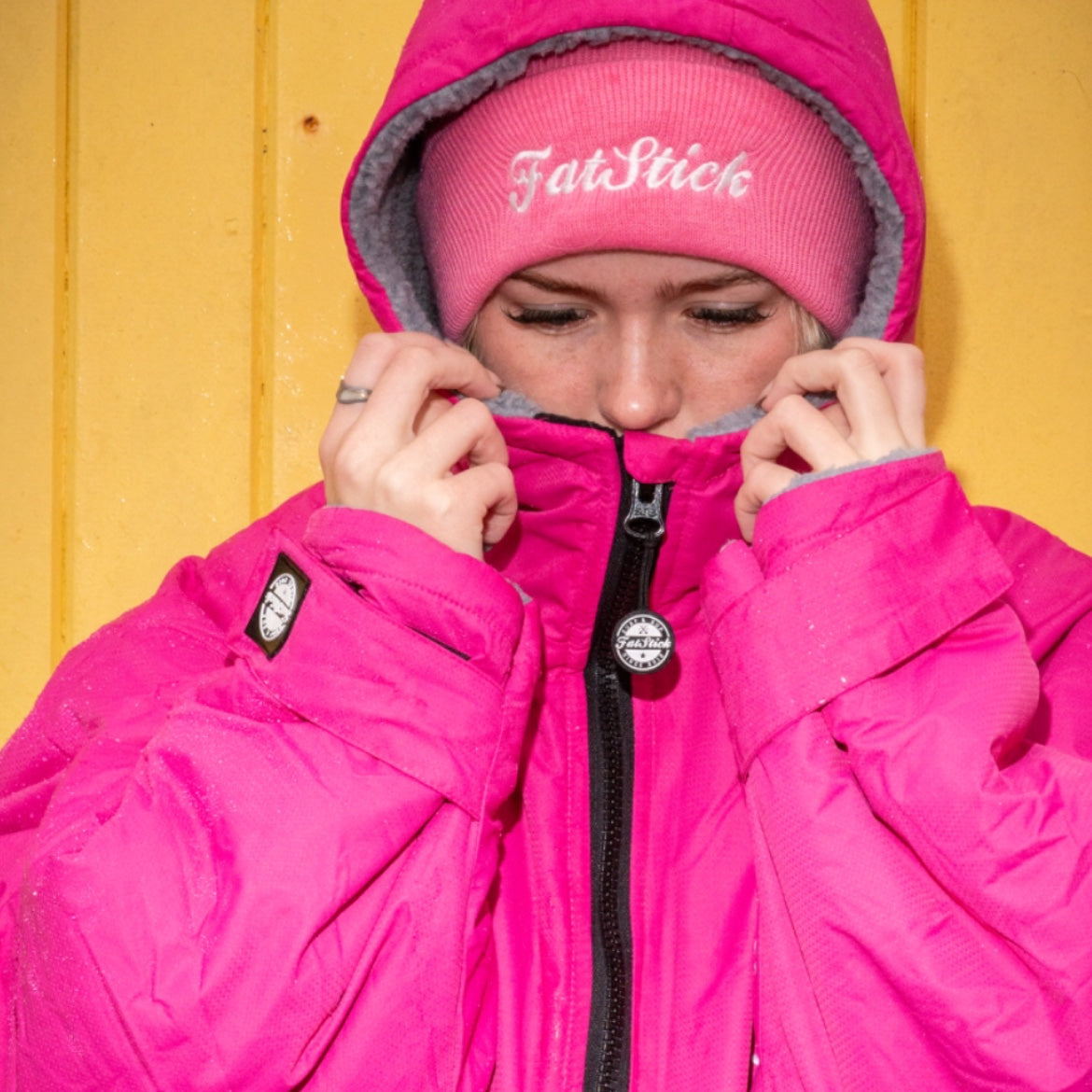 Woman in pink FatStick FatWrap changing robe and matching beanie, zipping up front.
