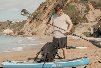 A man on a beach assembling the FatStick 4 Piece Carbon Shaft Paddle next to an inflatable paddle board.
