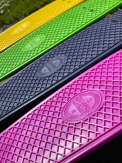 Close-up top view of the textured decks of four colorful FatStick Mini-Cruiser skateboards