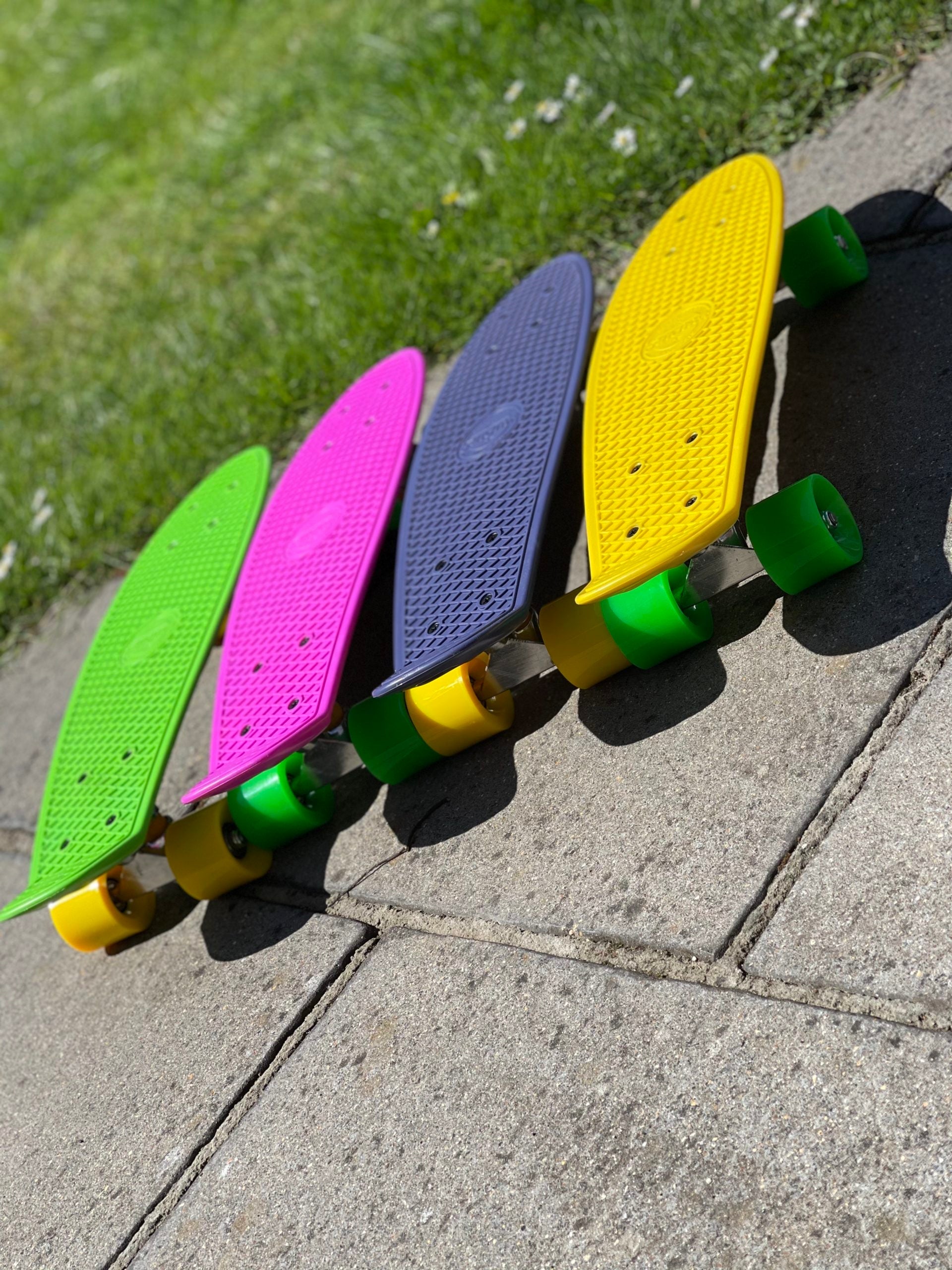 Angled top view of four colorful FatStick Mini-Cruiser skateboards lined up on pavement