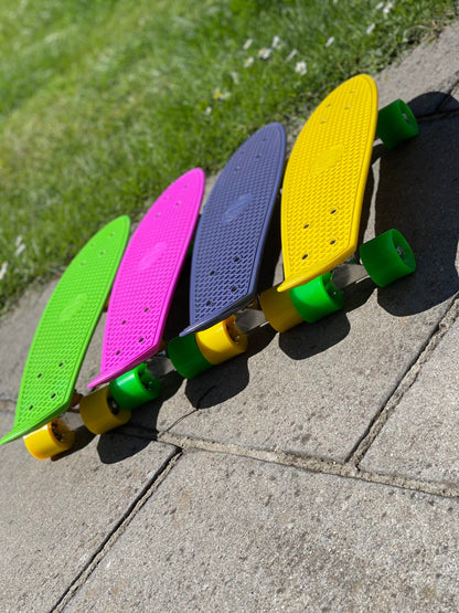 Angled top view of four colorful FatStick Mini-Cruiser skateboards lined up on pavement