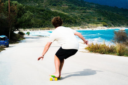 Front view of a person skateboarding a yellow FatStick Mini-Cruiser on a road by the ocean