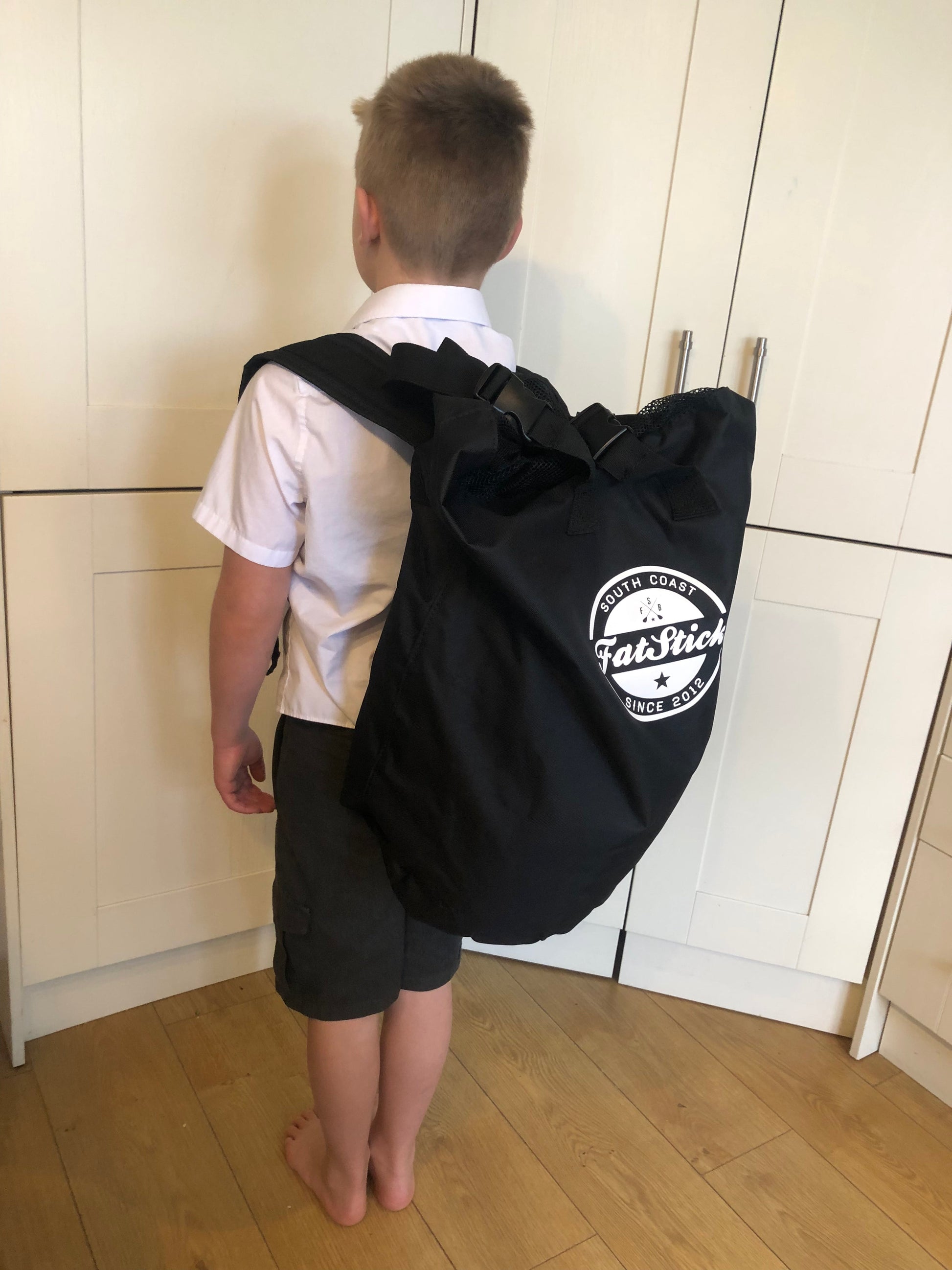 Young boy facing away, wearing a white shirt and dark shorts, carrying the packed Inflatable 43 Fatstick Body Board in a black backpack.