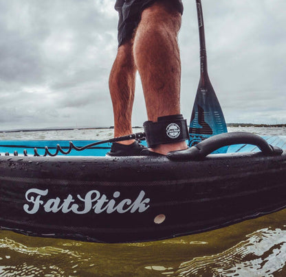 Person standing on a FatStick paddle board wearing the black coiled ankle leash