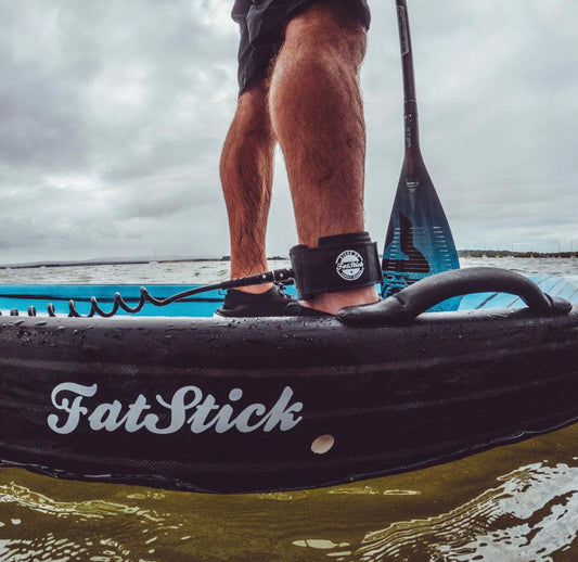 Person standing on a FatStick paddle board wearing the black coiled ankle leash