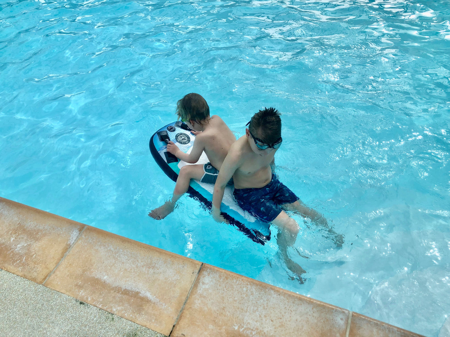 Two young boys in a swimming pool using the Inflatable 43 Fatstick Body Board, one sitting on it, the other next to it.
