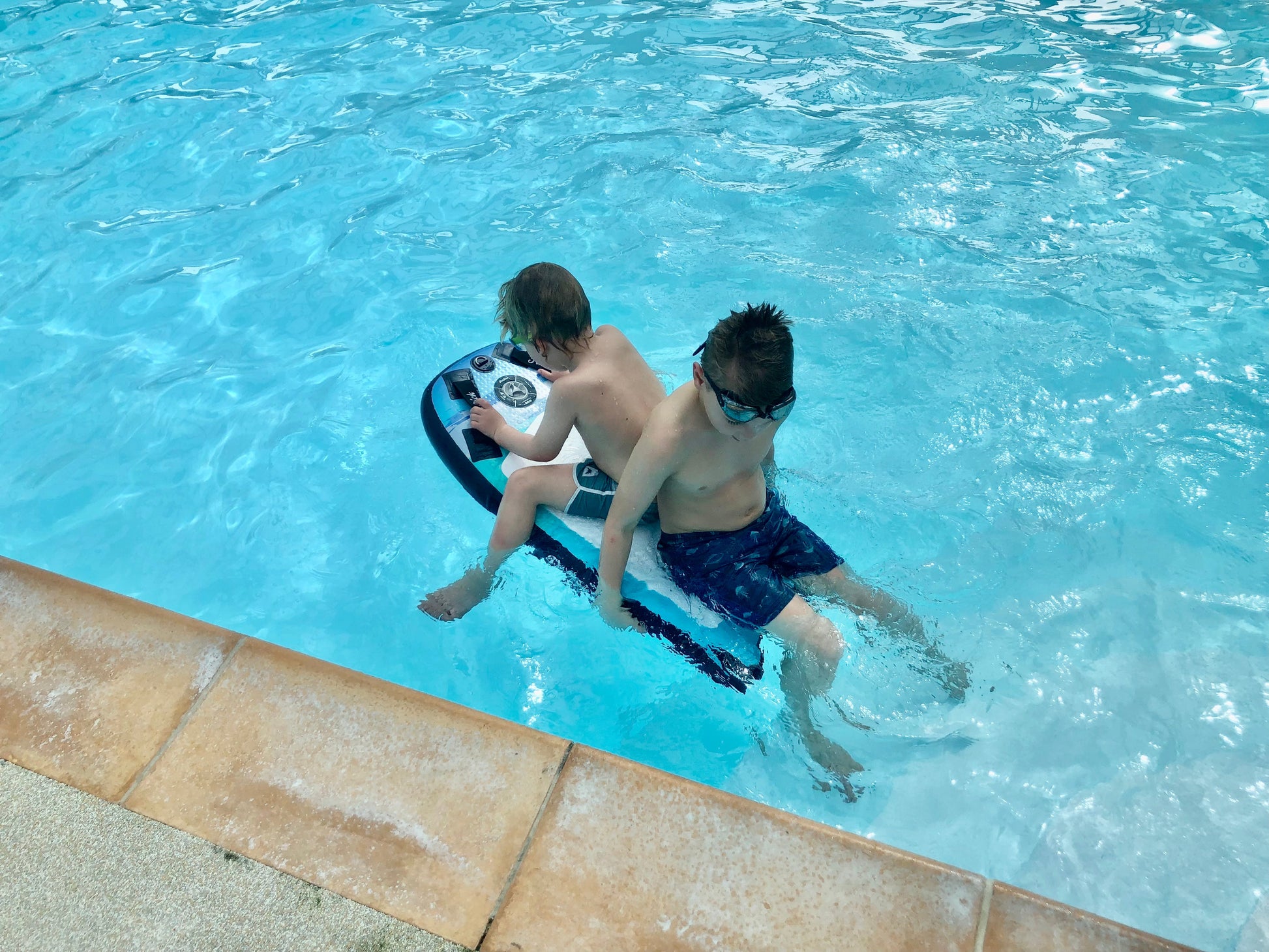 Two young boys in a swimming pool using the Inflatable 43 Fatstick Body Board, one sitting on it, the other next to it.