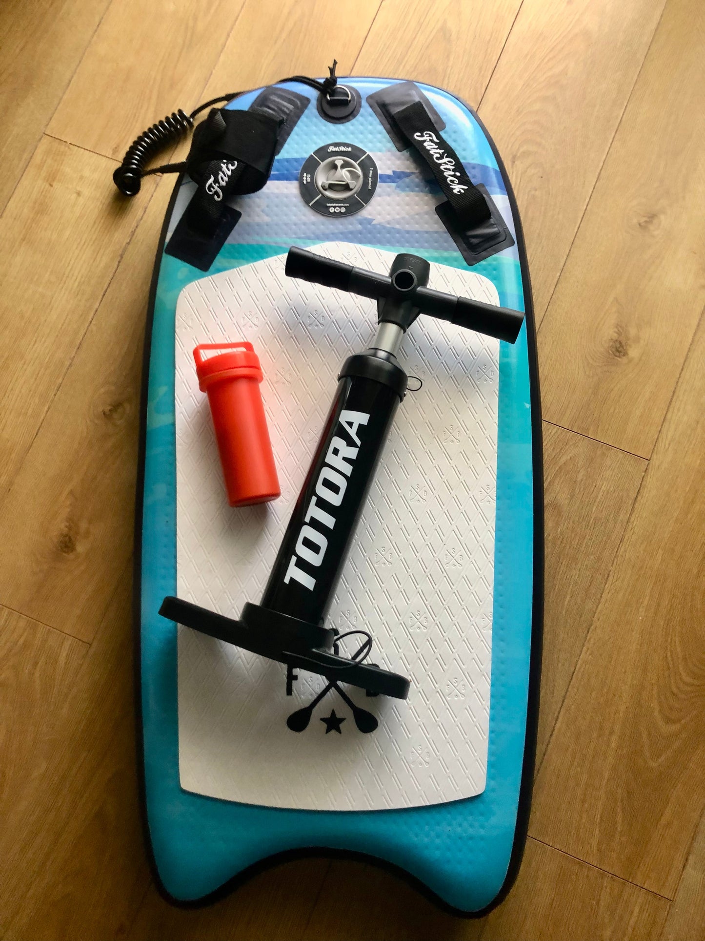 Black and red Totora pump and red bottle sitting on the white and blue Inflatable 43 Fatstick Body Board.