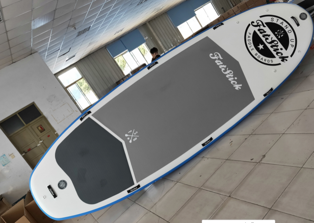 Overhead view of the XL Giant FatStick Paddle Board Package in a warehouse, showing the full deck with grey anti-slip pad and branding.