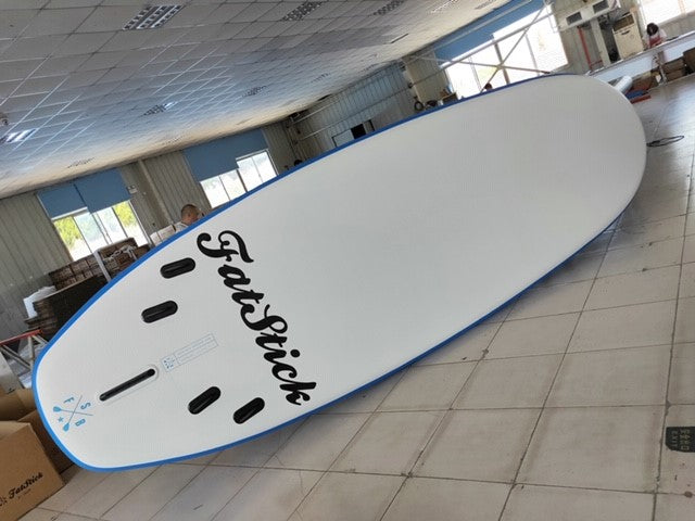 Bottom view of the XL Giant FatStick Paddle Board Package on a warehouse floor, displaying the white underside, blue trim, and fin boxes.